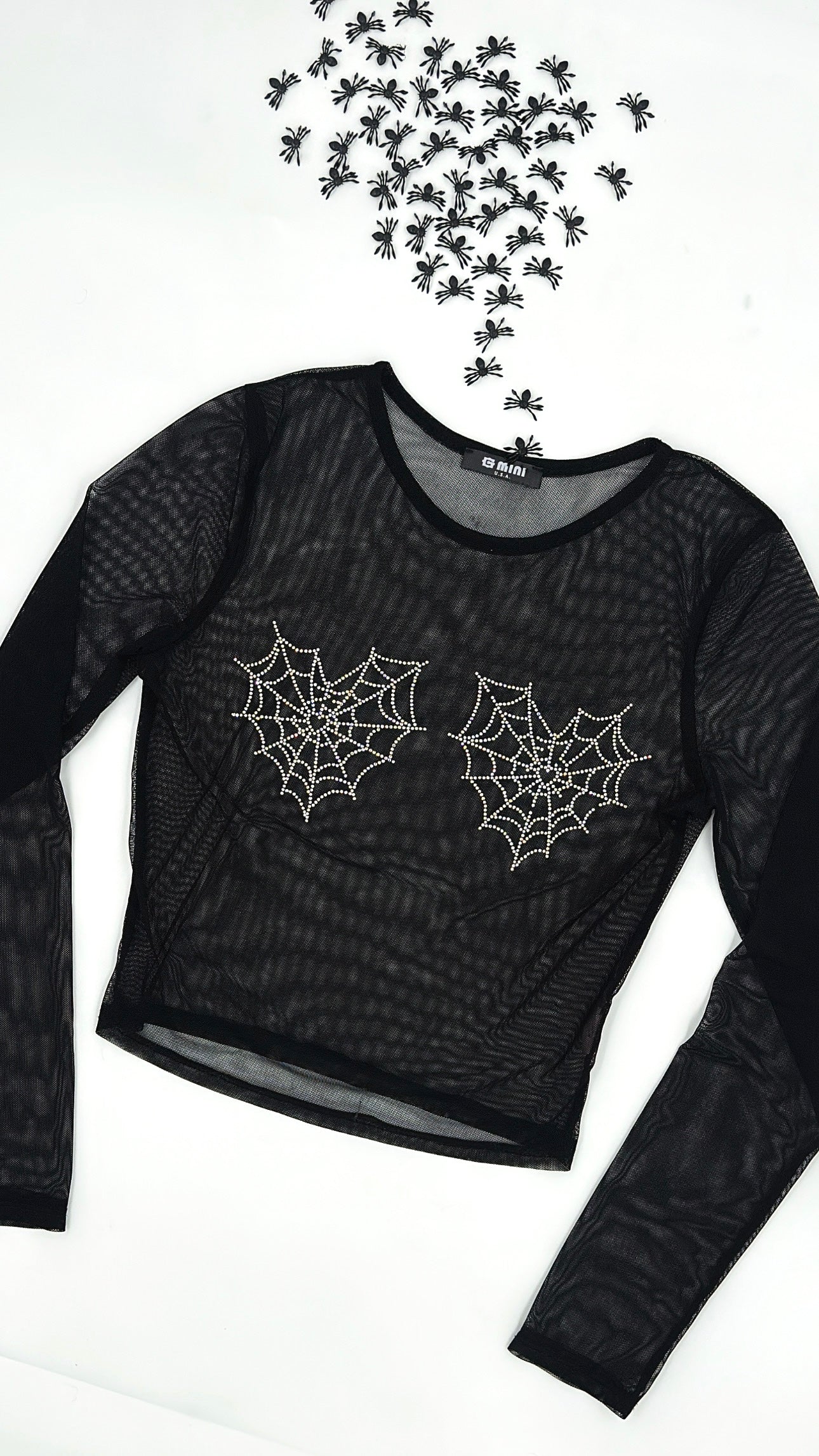 A black long-sleeve mesh top with a subtle snakeskin texture, featuring two white embroidered spiderwebs on the chest. The top is laid flat on a white background with a cluster of small black spider decorations arranged above it.