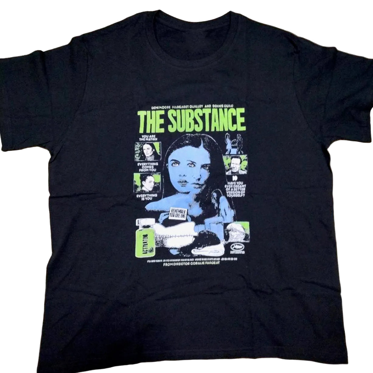 A black short-sleeve graphic t-shirt laid flat on a beige carpet. The shirt features a large front print for the movie 'The Substance' with lime green and blue graphics.